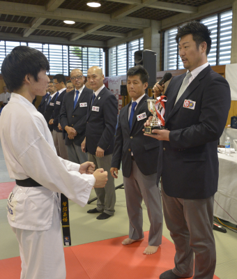 武道大会の表彰式で優勝トロフィーを贈呈する場面